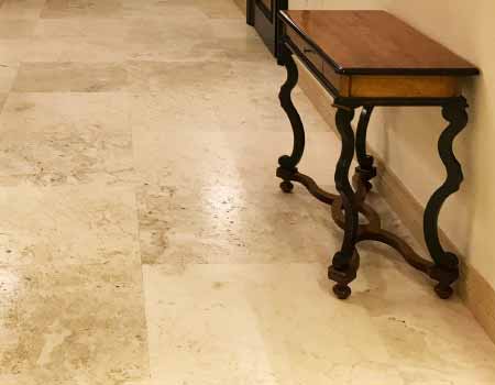 Mermer Silim Cilalama Restorasyon firmamızın traverten silim hizmeti için kullanılan görselde, kahverengi parlak bir traverten zemin üzerinde eski görünümlü estetik bir ahşap masa var.